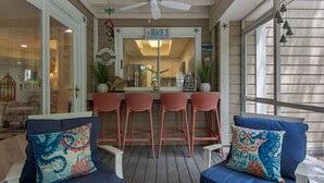 A covered outdoor seating area with a ceiling fan, a bar counter, and two bar stools. - Ground Floor Cottage with Free Beach Service! (Miramar Beach)