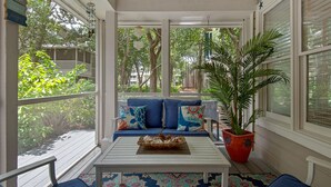 A covered porch with a white ceiling, blue cushions, a white table, and a large potted plant. - Ground Floor Cottage with Free Beach Service! (Miramar Beach)