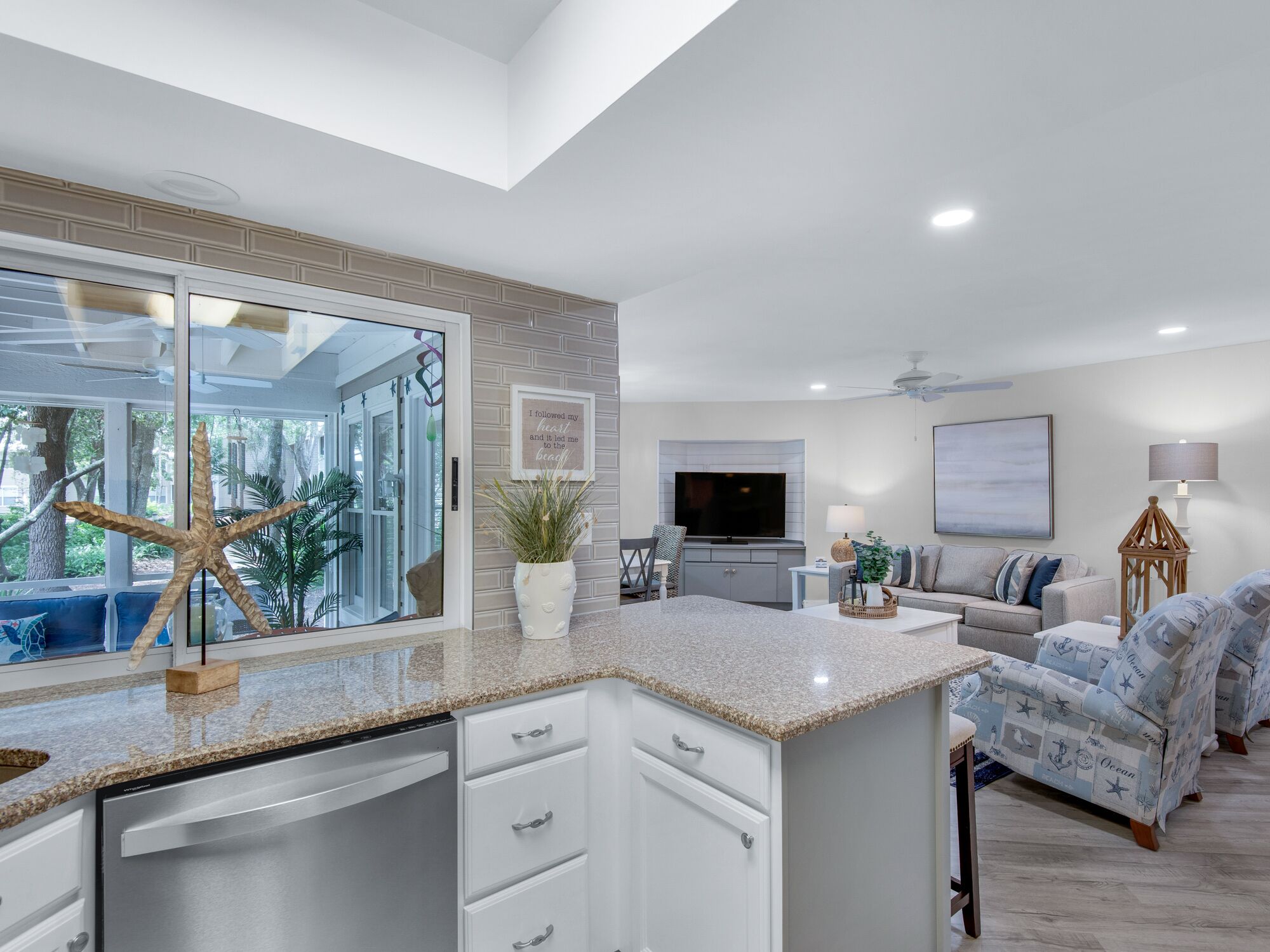 Una cocina moderna con una isla grande, un comedor con mobiliario con motivos marinos y una sala de estar con televisor y objetos decorativos.