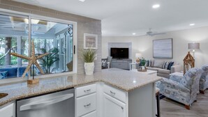 A modern kitchen with a large island, a dining area with ocean-themed furniture, and a living room with a TV and decorative items. - Ground Floor Cottage with Free Beach Service! (Miramar Beach)