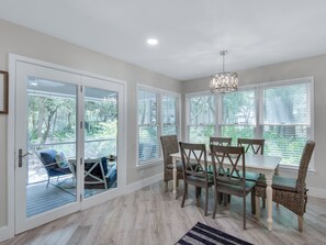 A dining area with a table and chairs, large windows with blinds, and a ceiling fan.
