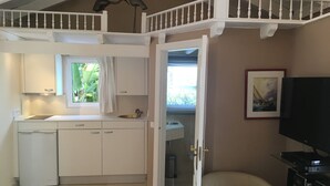 Una cocina compacta con lavavajillas, un lavamanos y un ventanal con cortinas. También se ve una silla y un televisor de pantalla plana.