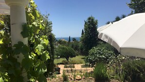 Un jardín con una sombrilla blanca, una silla lounge a rayas y vistas al mar.