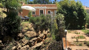 Una casa con techo de tejas, rodeada de exuberante vegetación y un paisaje rocoso.