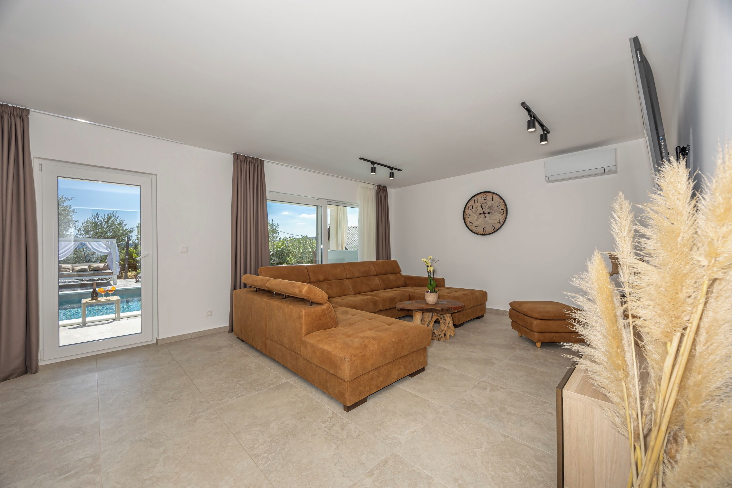 A spacious living room with a large sectional sofa, a coffee table, and a view of a swimming pool through a sliding glass door.
