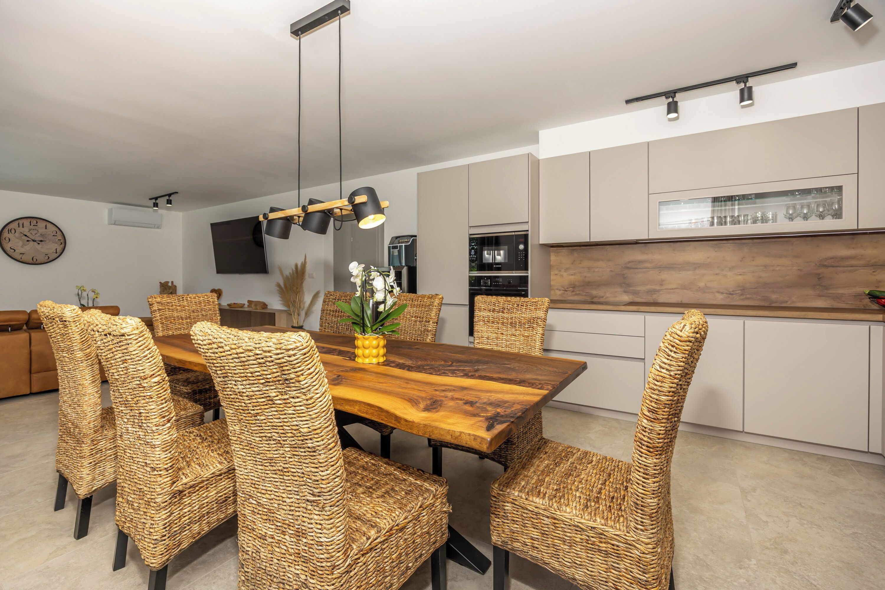 A modern kitchen with a dining area featuring a wooden table and woven chairs.