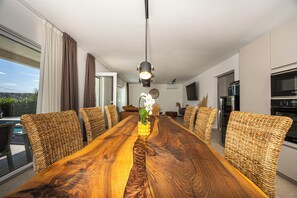 Une salle à manger moderne avec une longue table en bois, des chaises en osier et un vase rempli de fleurs.