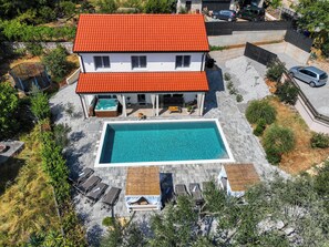 Una casa de dos pisos con piscina, mobiliario exterior y jardín.
