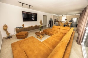 A modern living room with a large sectional sofa, a flat-screen TV mounted on the wall, and a kitchen area visible through an open doorway. - VILLA VALENTINA -Luxury Stay for 8+1 Guests with XXL Pool&Whirlpool (Bribir)