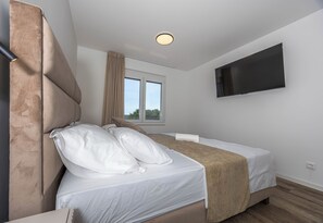 Un dormitorio con cama, televisor montado en la pared y ventana con cortinas.
