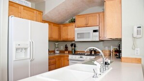 A kitchen with wooden cabinets, a white refrigerator, a microwave, a stove, and a sink.
