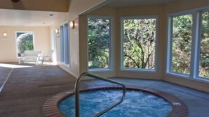 A hot tub with a metal ladder, surrounded by windows with a view of greenery.