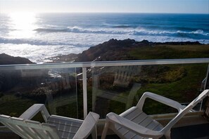 Enjoy the ocean view from this balcony with glass railings, featuring two chairs for taking in the scenery.