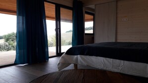 Une chambre avec un lit, un plancher en bois et une vue sur l’extérieur, accessible par une porte-fenêtre coulissante.