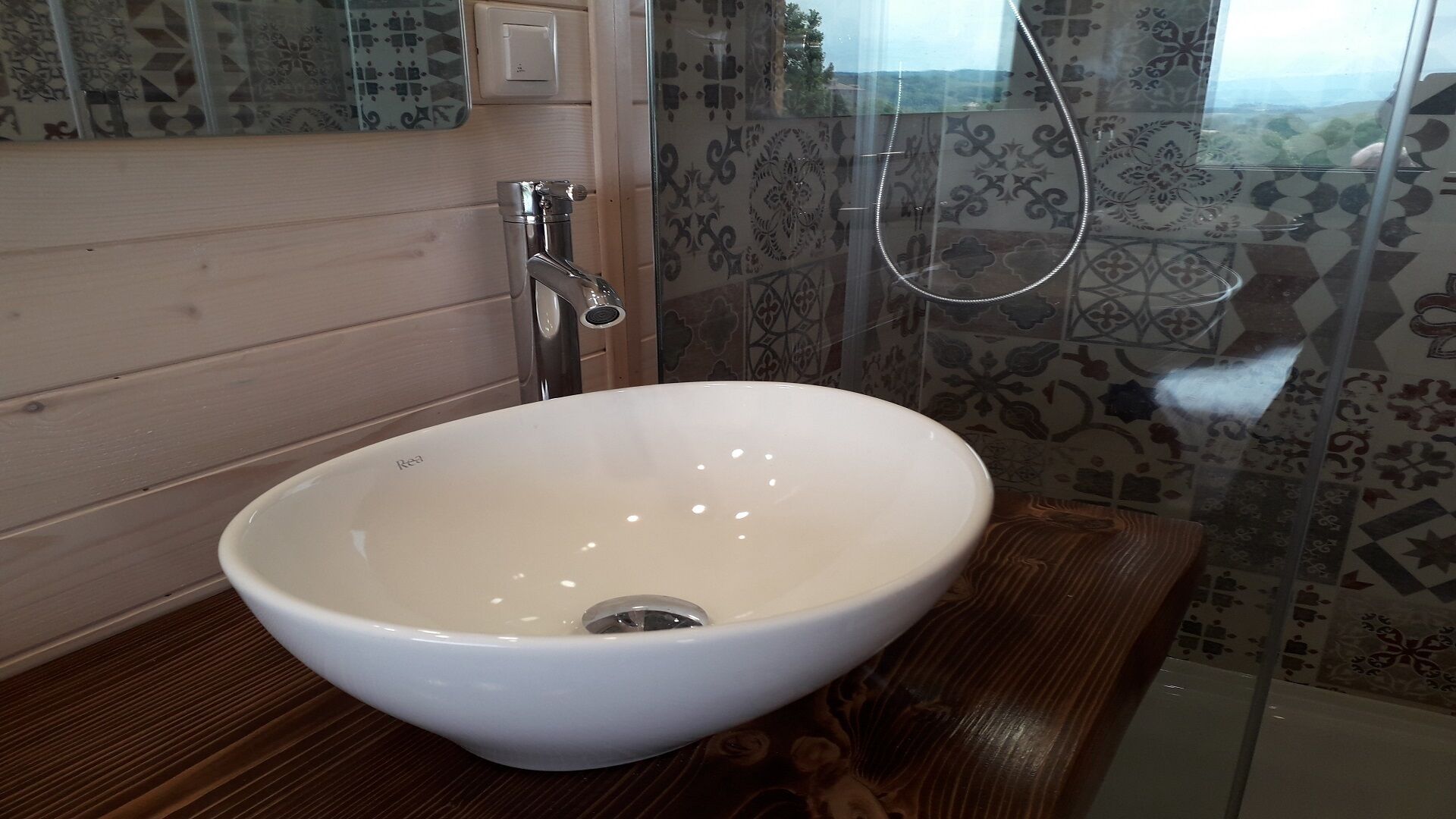 Une salle de bain avec un lavabo blanc, un meuble-lavabo en bois, des carreaux à motifs et un espace douche.