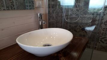 Une salle de bain avec un lavabo blanc, un meuble-lavabo en bois, des carreaux à motifs et un espace douche.