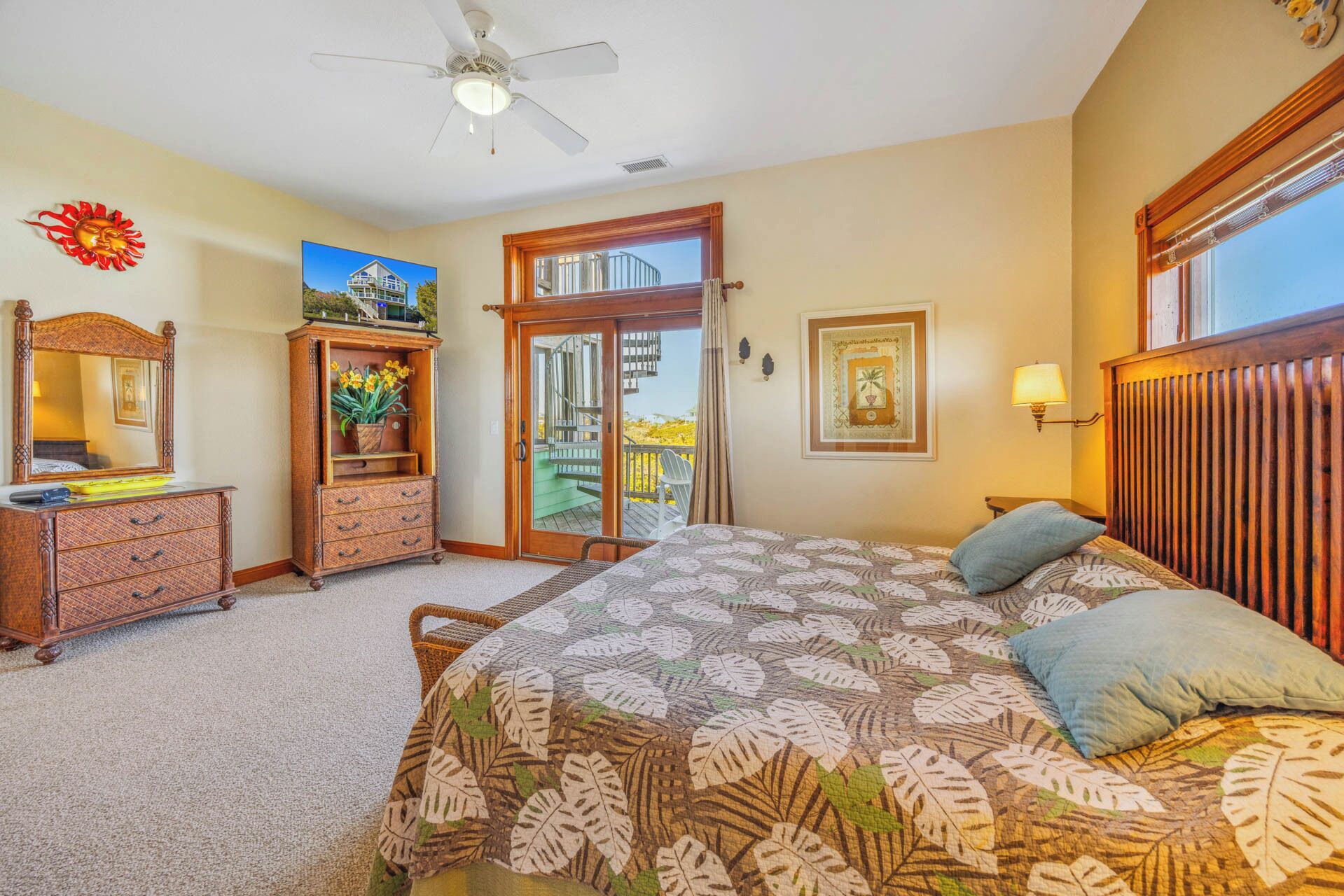 A bedroom with a bed, a dresser, a mirror, a ceiling fan, and a balcony door.