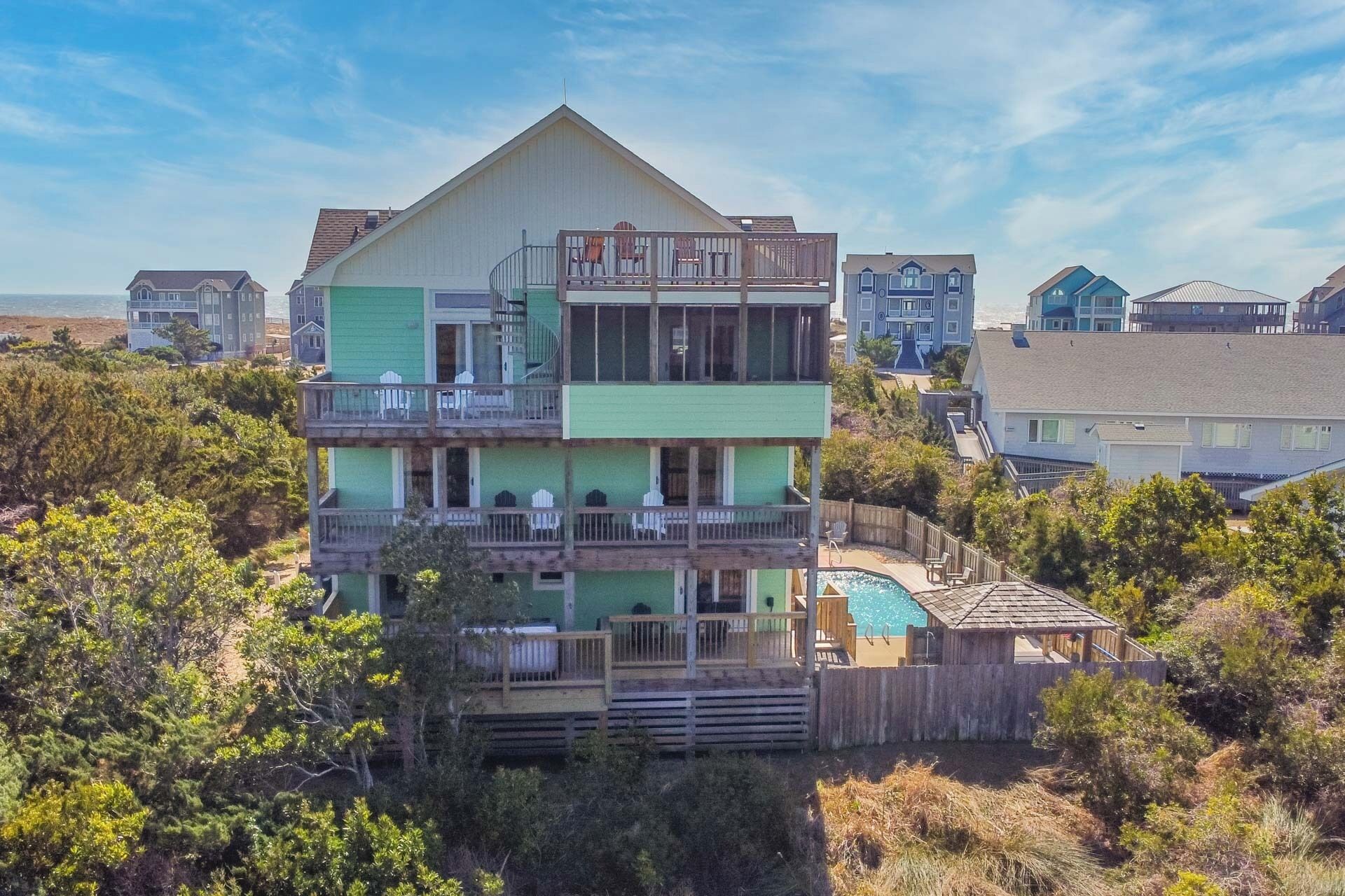 Una casa frente al mar de varios pisos, con piscina, balcones y una terraza de madera.