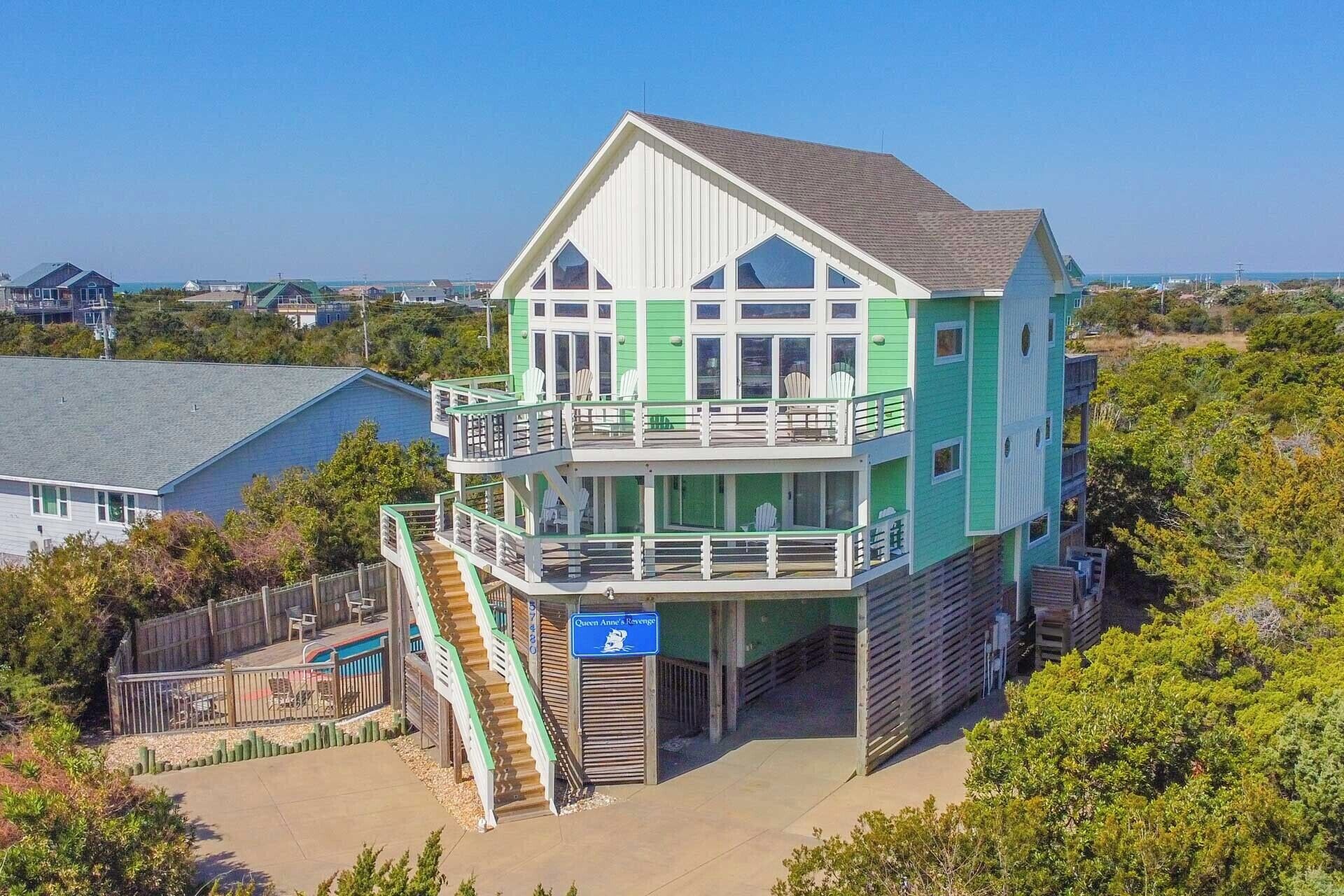 A two-story beachfront house with a balcony, a staircase leading to the entrance, and a sign indicating the name "Queen Anne's Revenge".