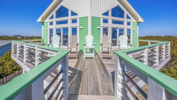 A white and green wooden structure with multiple windows and a deck in front.