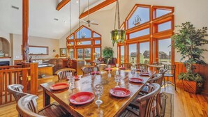 A spacious dining area with a large wooden table set for a meal, surrounded by wooden chairs.