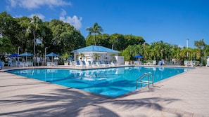 A swimming pool with lounge chairs and umbrellas, surrounded by trees and a covered pavilion.