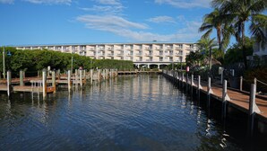 A waterfront hotel with a long dock extending into calm water, surrounded by lush greenery and a clear blue sky. - Ocean View 2BR Pool, Private Beach (Tavernier)