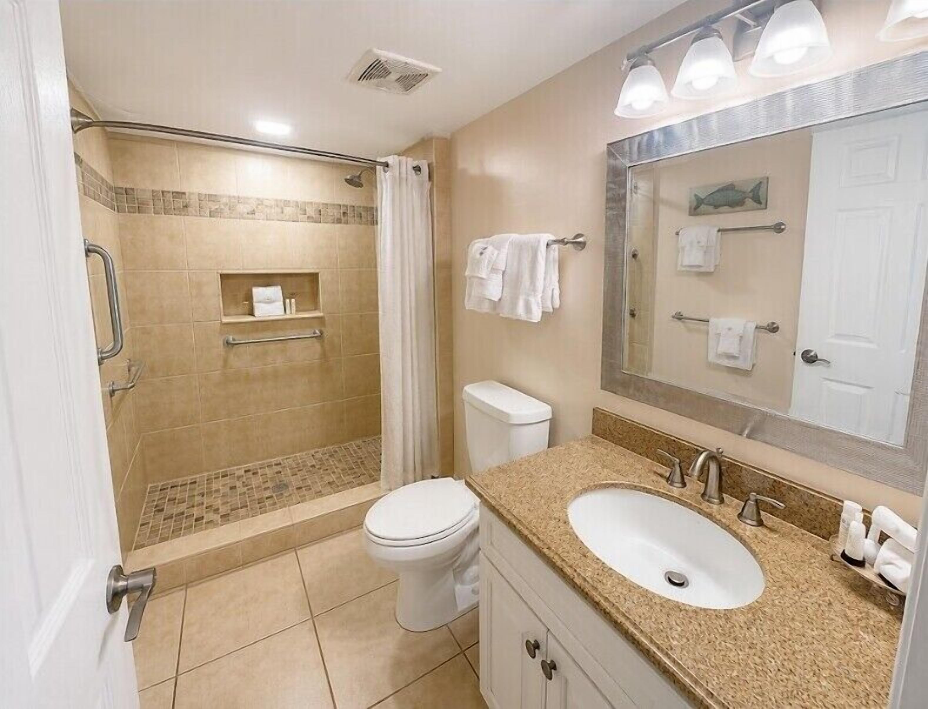 A bathroom with a shower, toilet, sink, and a mirror with a towel rack.