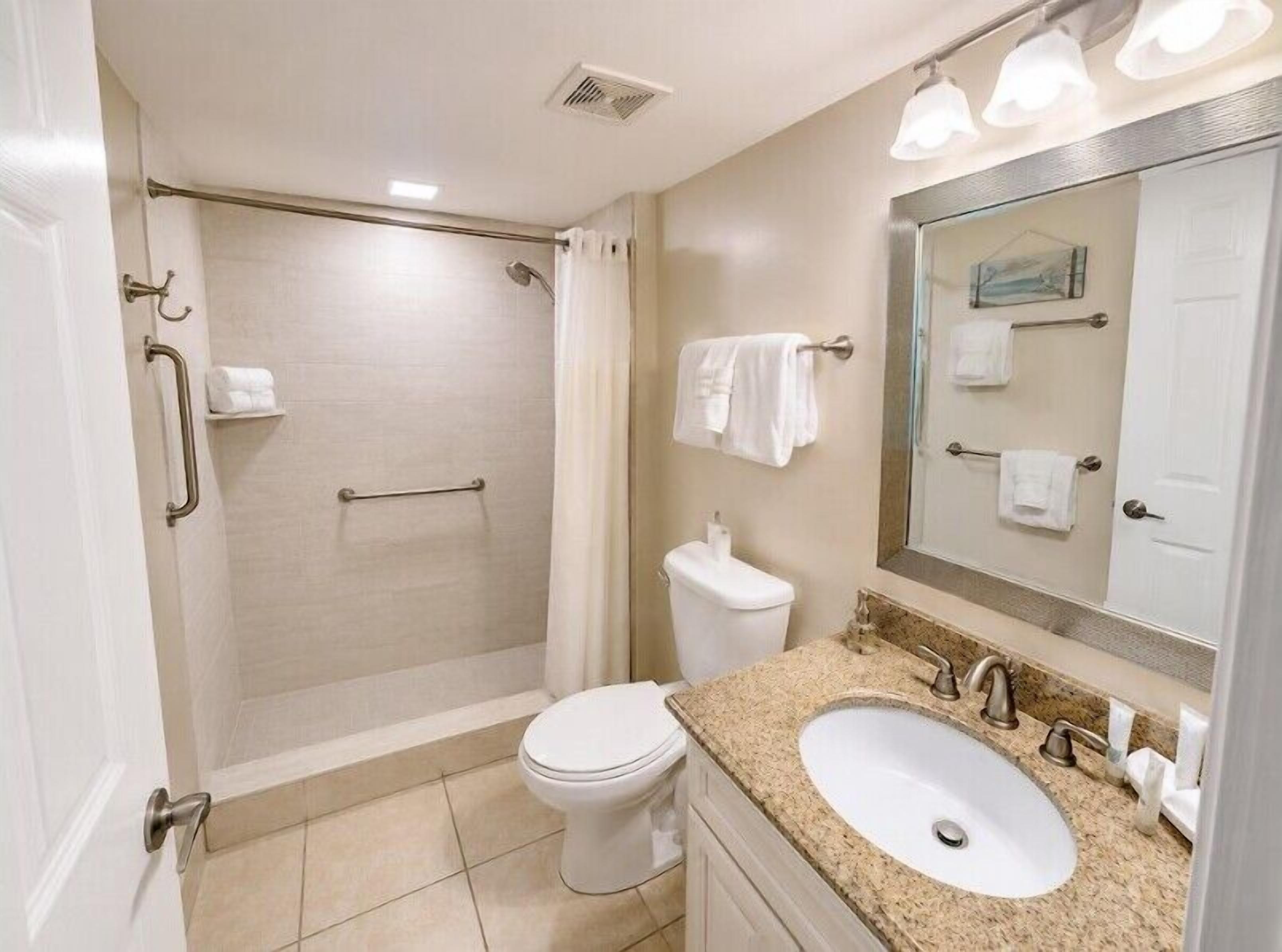 Une salle de bain équipée d’une douche, de toilettes, d’un lavabo et d’un grand miroir.