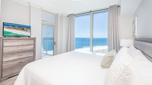 Une chambre d’hôtel avec un grand lit, un téléviseur posé sur une commode en bois et une vue sur l’océan.
