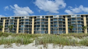 Un hotel de varios pisos con balcones y una playa arenosa en primer plano.