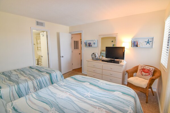 A bedroom with two beds, a dresser, a television, and a chair.