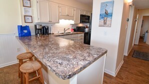 Una cocina con armarios blancos, encimera de granito y refrigerador de acero inoxidable.