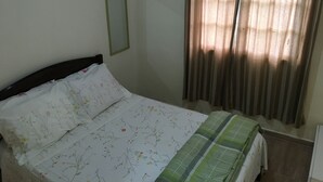 Un dormitorio con cama, espejo y ventana con cortinas.