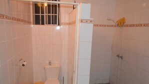 Kylpyhuone, jossa on wc, suihku ja laatoitettu lattia.
