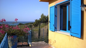 A balcony with a view of the sea, a potted plant with pink flowers, and a building with blue shutters. - Cozy Studio Erato ideal for a couple (Menfi)