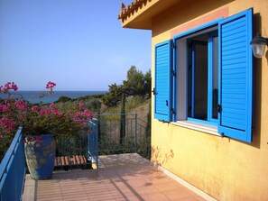 A balcony with a view of the sea, a potted plant with pink flowers, and a building with blue shutters. - Cozy Studio Erato ideal for a couple (Menfi)