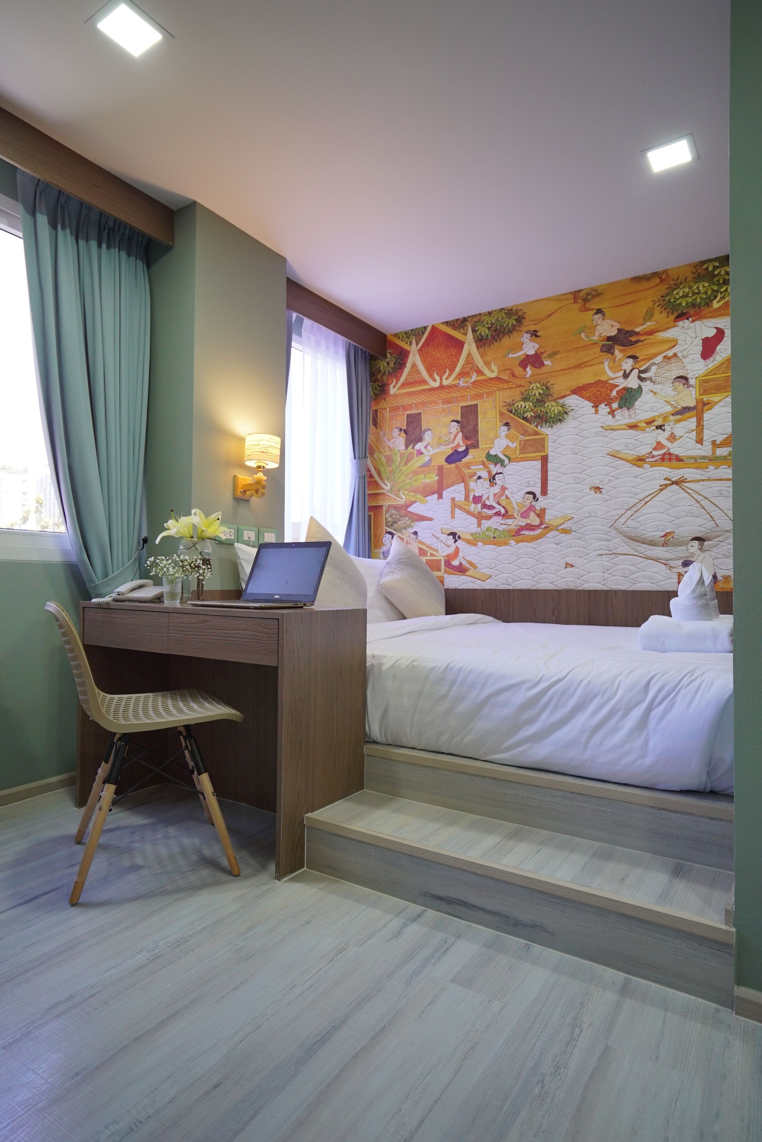 Habitación de hotel con cama, escritorio, ordenador portátil, silla y un mural en la pared.