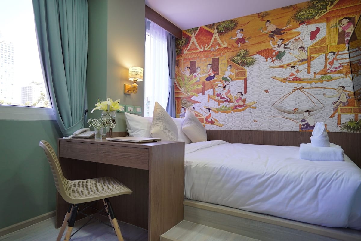 A hotel room with a bed, desk, chair, and a mural on the wall.