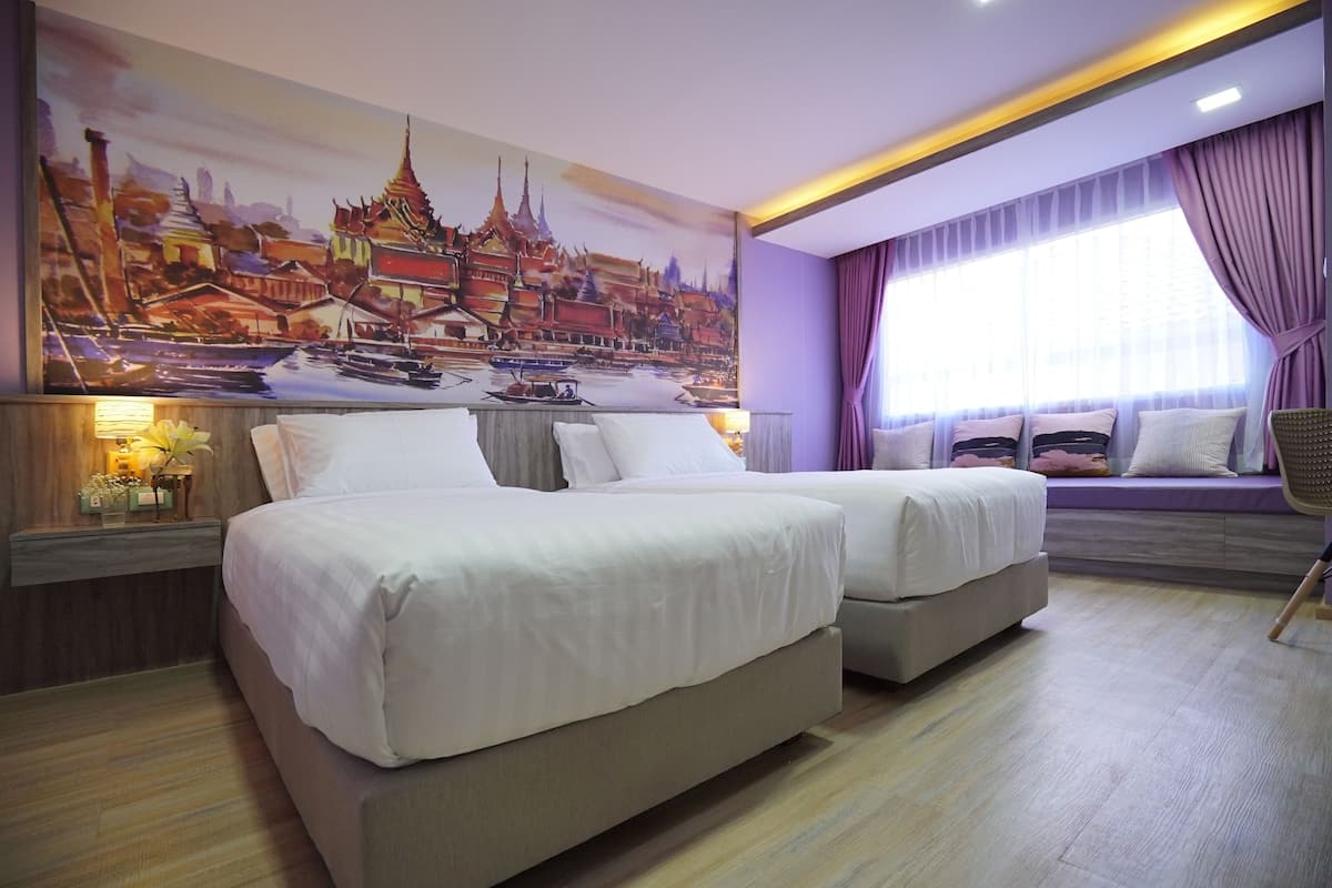 A hotel room with two beds, a large mural of a cityscape, a window with purple curtains, and a wooden floor.