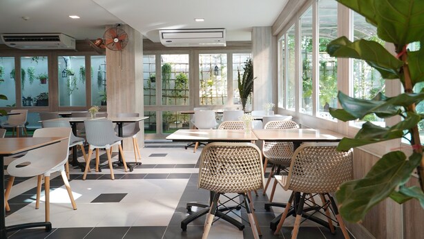 Een moderne binnenruimte met tafels en stoelen, grote ramen en kamerplanten.