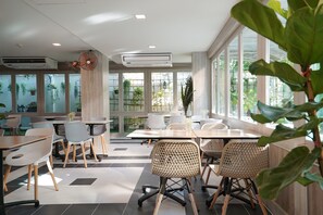 A modern indoor space with tables and chairs, large windows, and indoor plants. - The Qube Fifty Hotel (Bangkok)