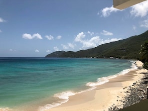 A beach with clear turquoise water, a sandy shore, and a mountainous backdrop.