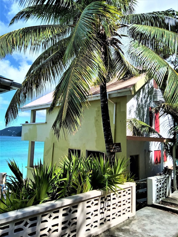 A two-story building with a balcony, surrounded by lush greenery and a view of the sea.