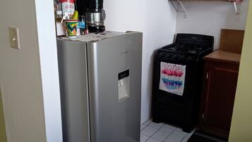 Une cuisine compacte équipée d’un réfrigérateur en acier inoxydable, d’une cuisinière à gaz et d’un four à micro-ondes. Des étagères situées au-dessus de la cuisinière servent à ranger divers ustensiles de cuisine.