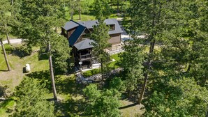 Eine Holzhütte mit einer großen Terrasse und einer Steinmauer, umgeben von dichtem Wald.
