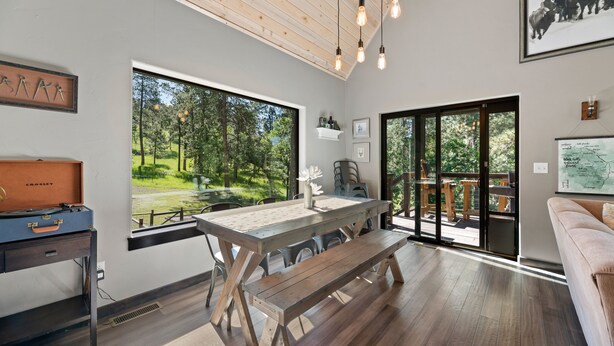 Ein modernes Interieur mit Holztisch und Bank, großen Fenstern mit Blick auf Grünflächen und einer gemütlichen Sitzecke.