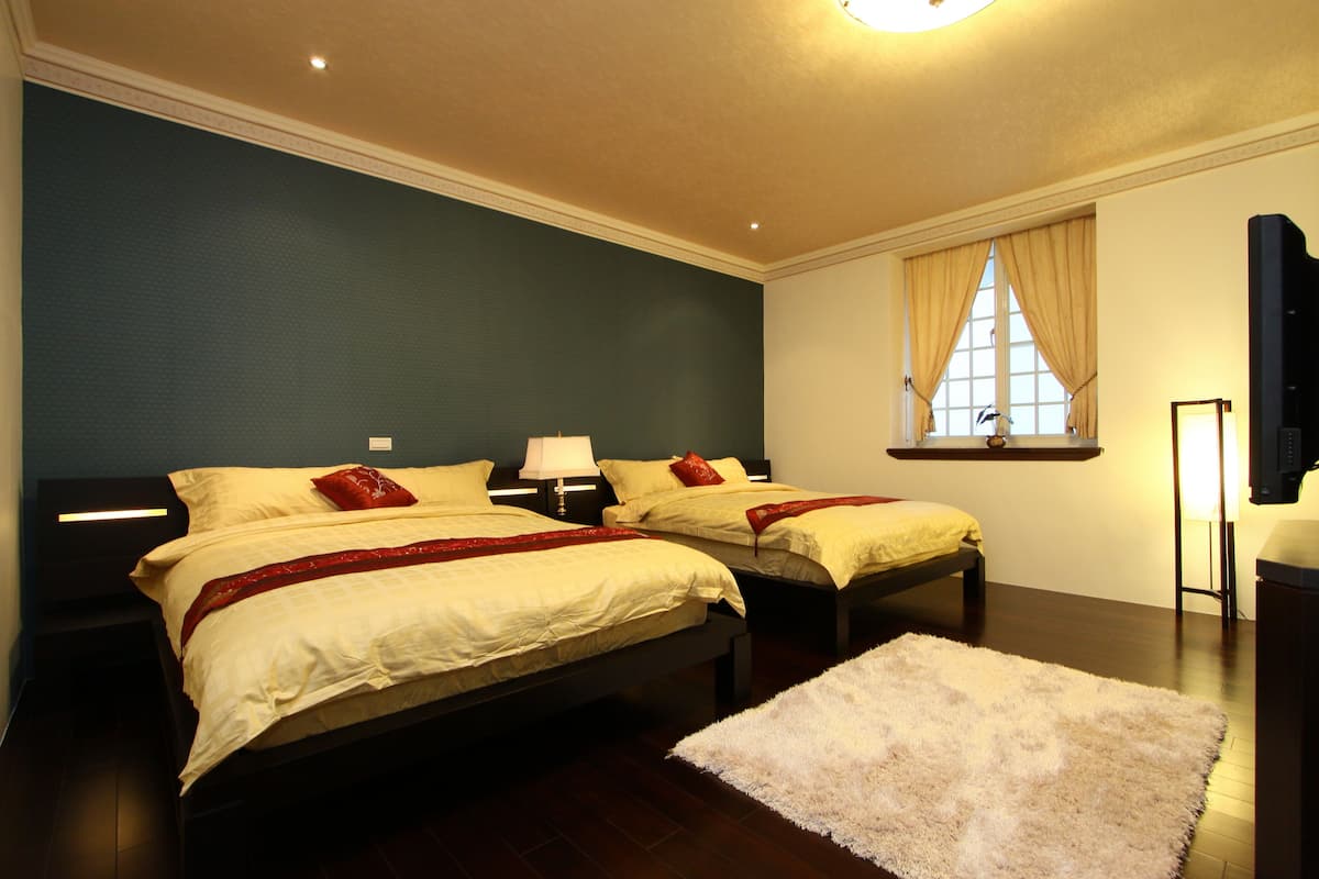 Habitación de hotel con dos camas, un ventanal con cortinas, un televisor de pantalla plana y una alfombra blanca.