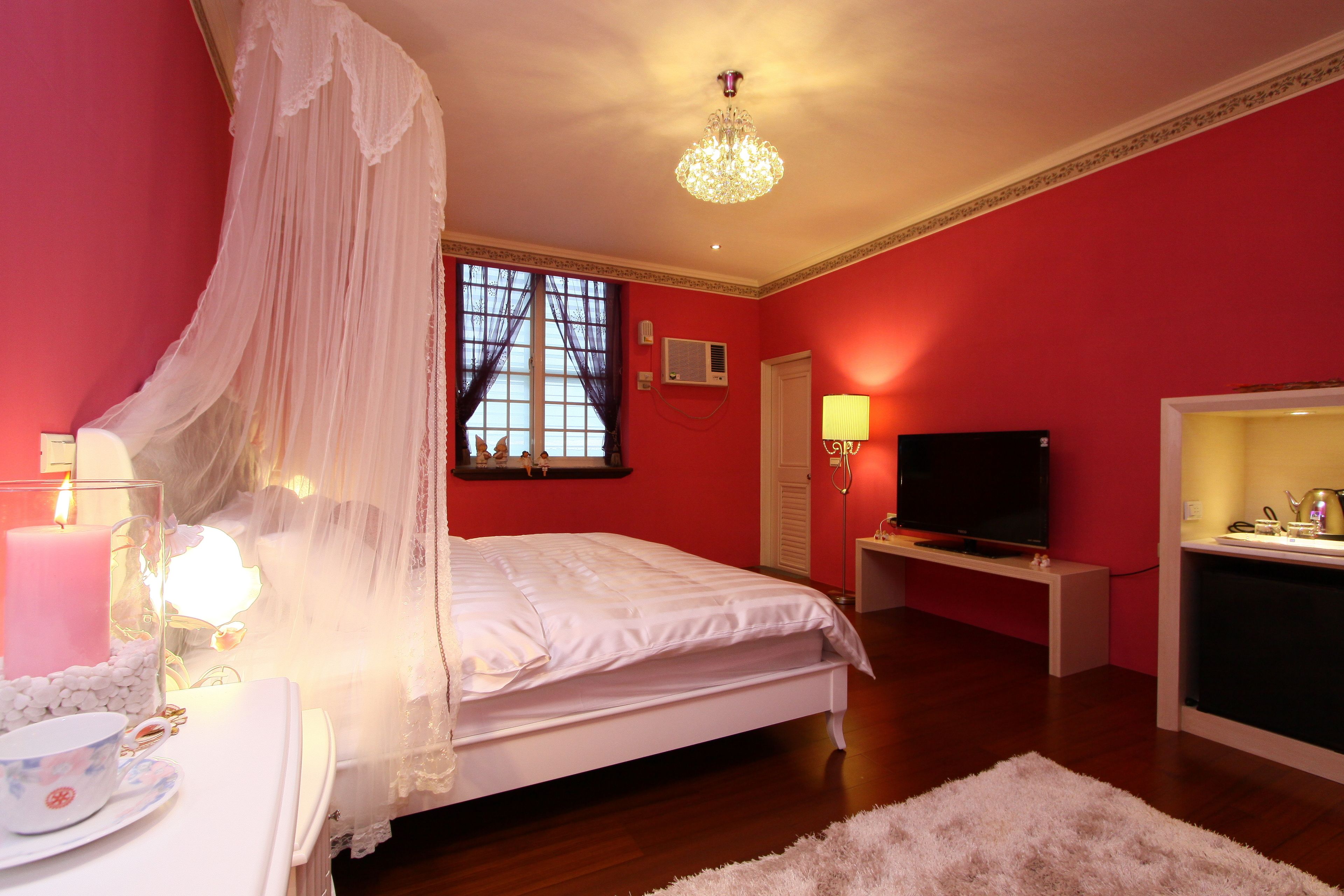 Une chambre à coucher avec un lit, une télévision, une table de chevet, une lampe et une fenêtre avec des rideaux.