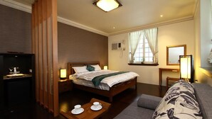 Een hotelkamer met een bed, nachtkastje met bekers, een bank, een bureau met lamp, een spiegel en een raam met gordijnen.